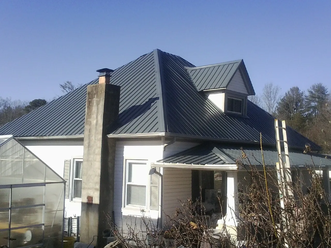 Dark blue standing seam metal roof on a white farmhouse with dormer — Slate & Tile Roof Repair by Roofing Brothers in Griffithsville