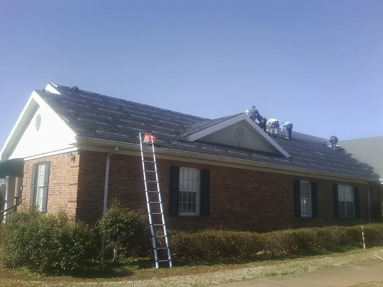 Crew tearing shingles off a brick ranch roof with a ladder set — Metal Roof Repair work by our crew in Griffithsville