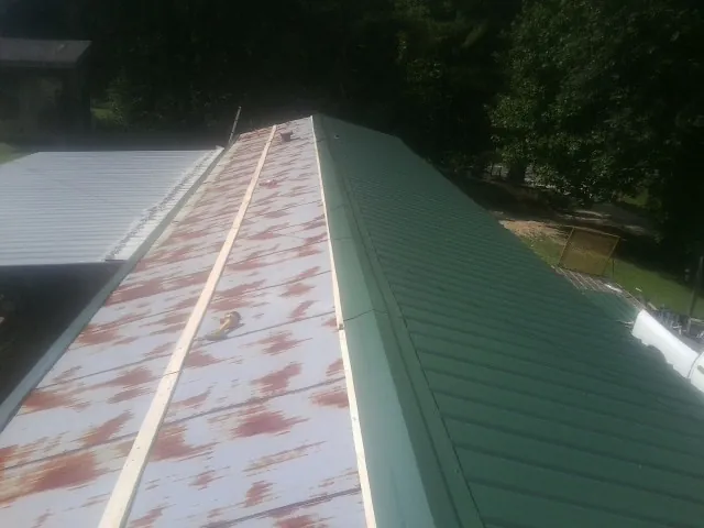 Old rusted panels beside newly installed green metal roofing — Wind Damage Roof Repair by Roofing Brothers in Griffithsville
