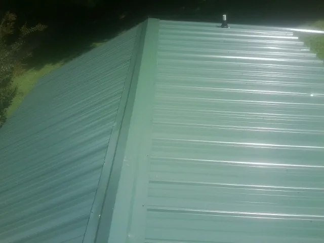 New green metal panels meeting at the ridge of a roof — Flat Roof Repair work by our crew in Griffithsville