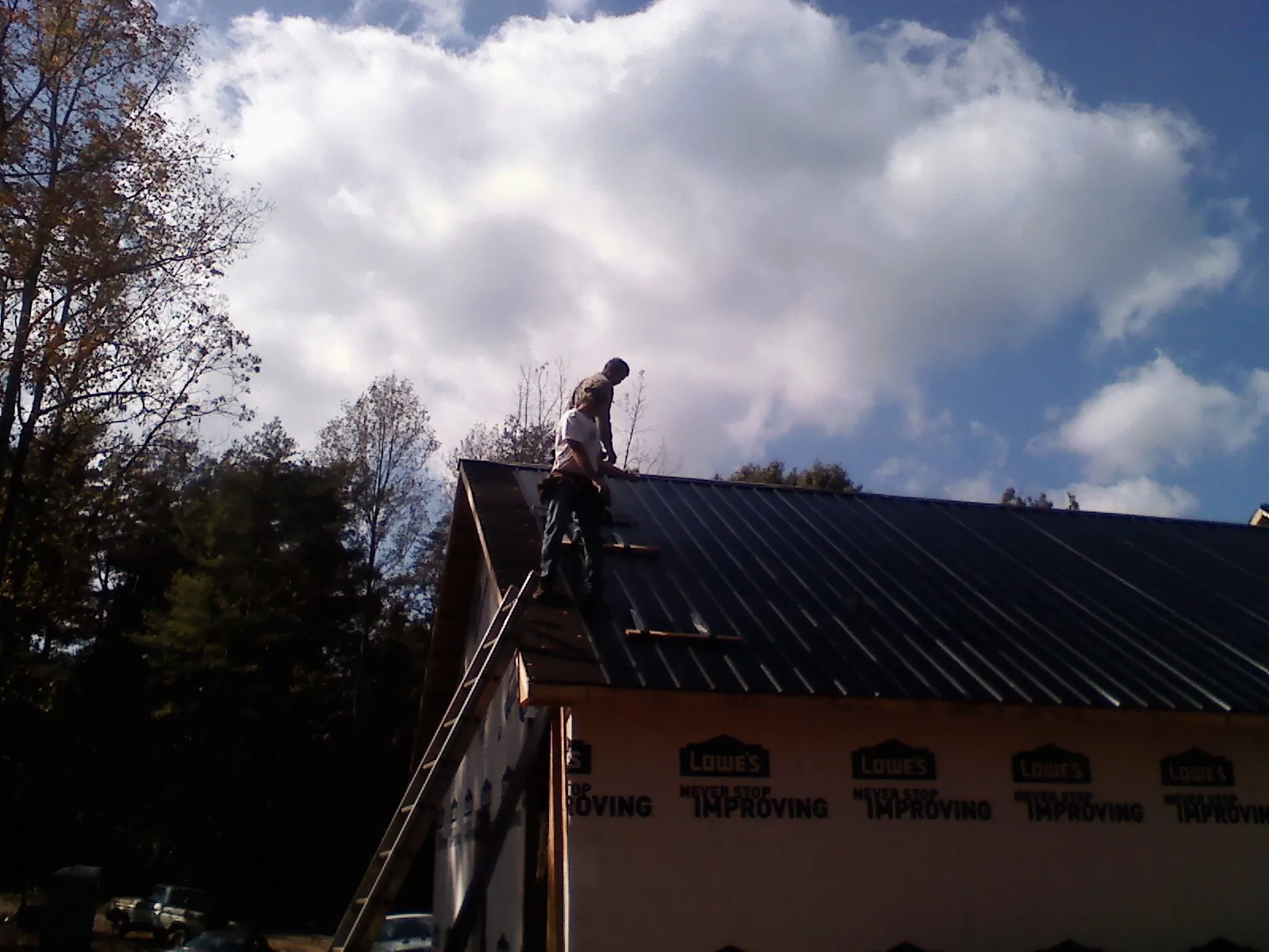 Roofer fastening dark metal panels high against a cloudy sky, from a Roof Inspection job in Griffithsville