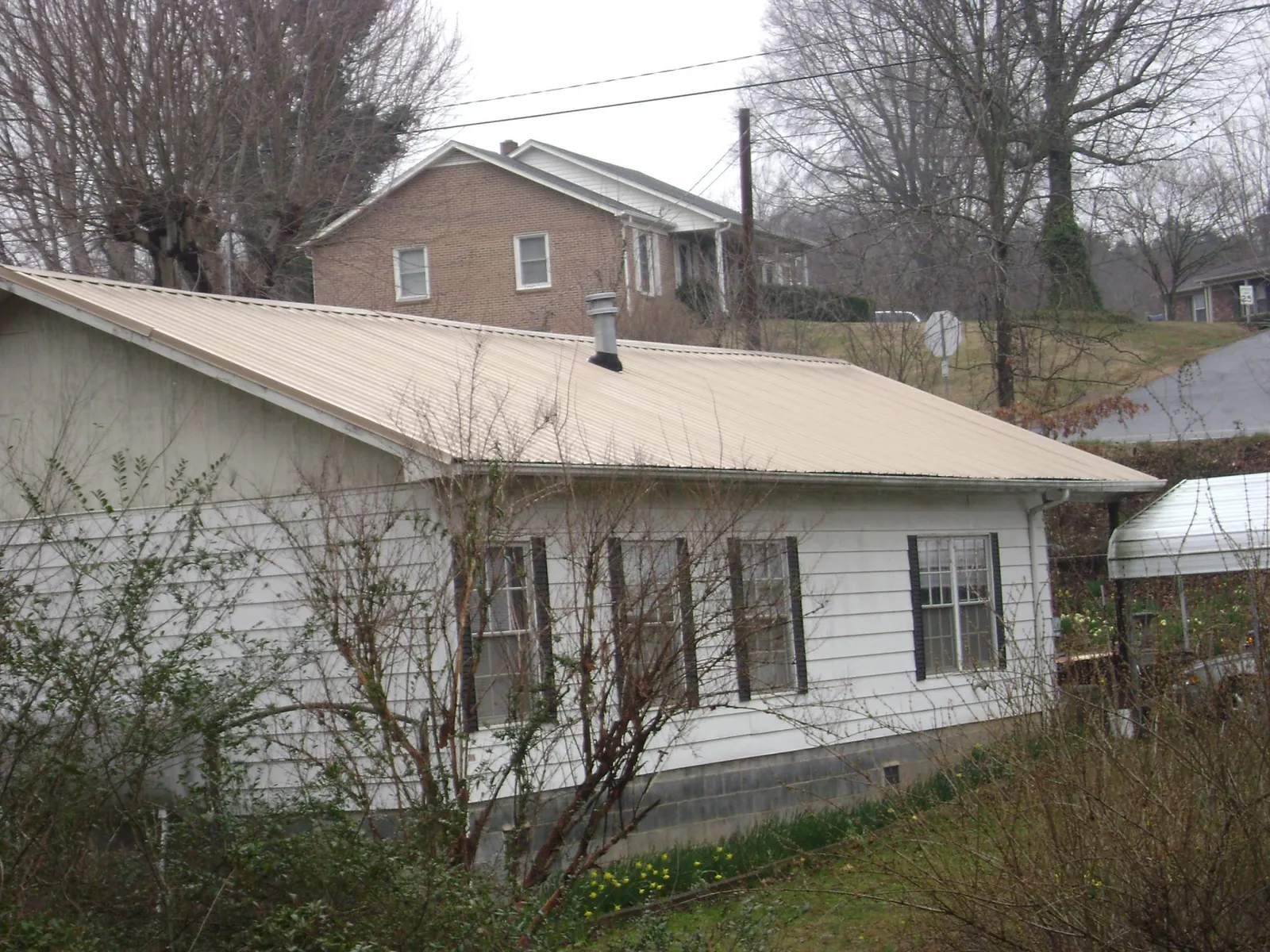 Tan metal roof on a white sided house set into a hillside — Commercial Roofing by Roofing Brothers in Griffithsville