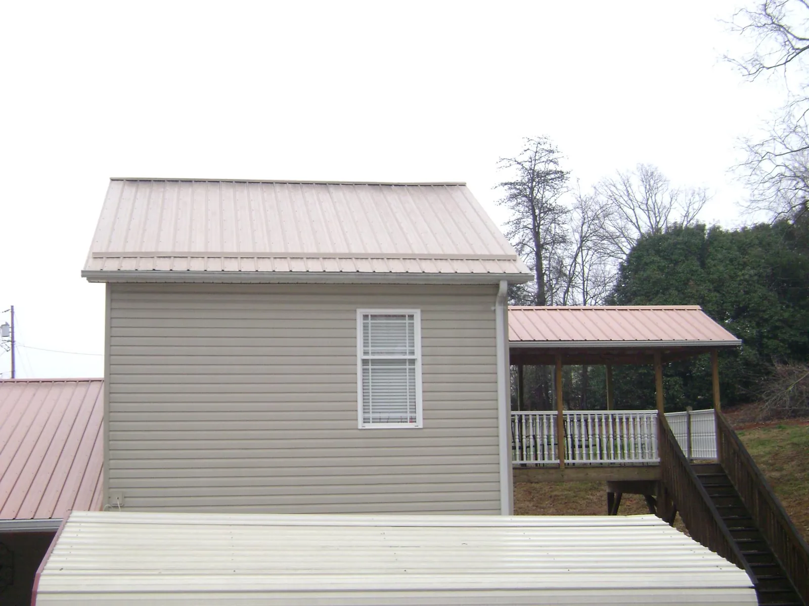 Tan metal roofs on a two story addition and attached porch, from a Roof Replacement job in Griffithsville